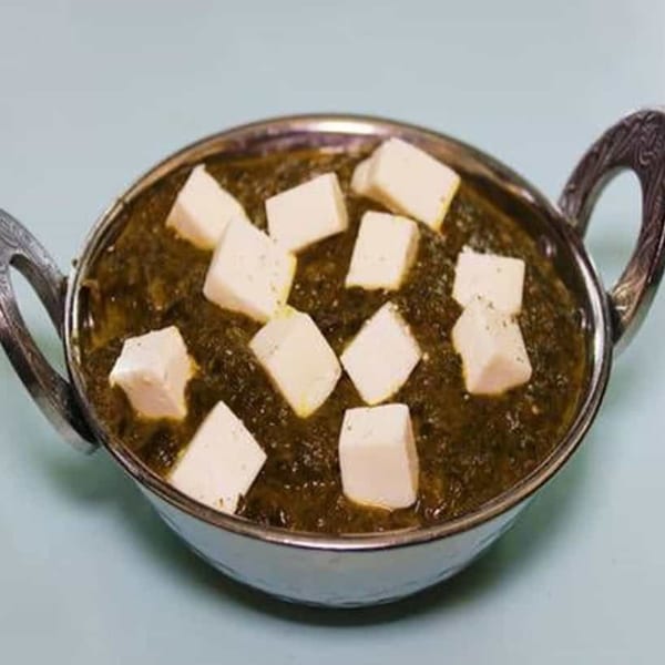 Palak Paneer, an Indian dish with spinach gravy and paneer cheese cubes, in a metal bowl.