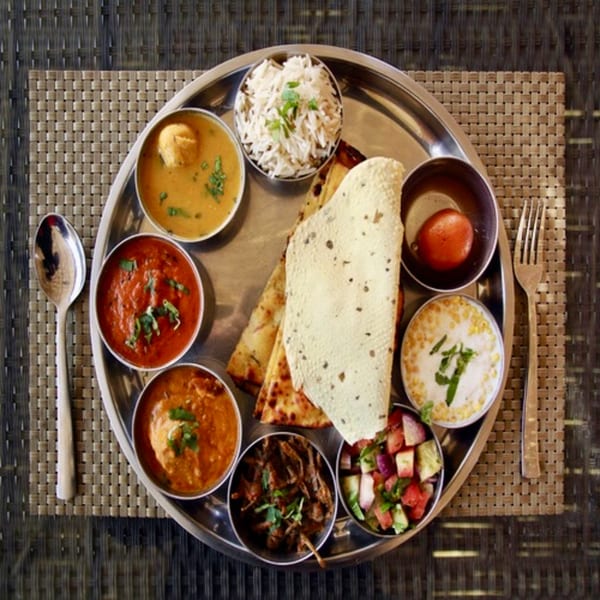 Overhead view of an Indian thali with various dishes, rice, bread, and dessert on a metal platter.