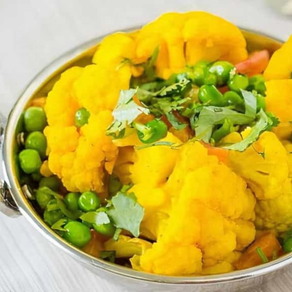 Close-up of a vibrant Indian dish with yellow cauliflower, green peas, and fresh cilantro in a silver bowl.