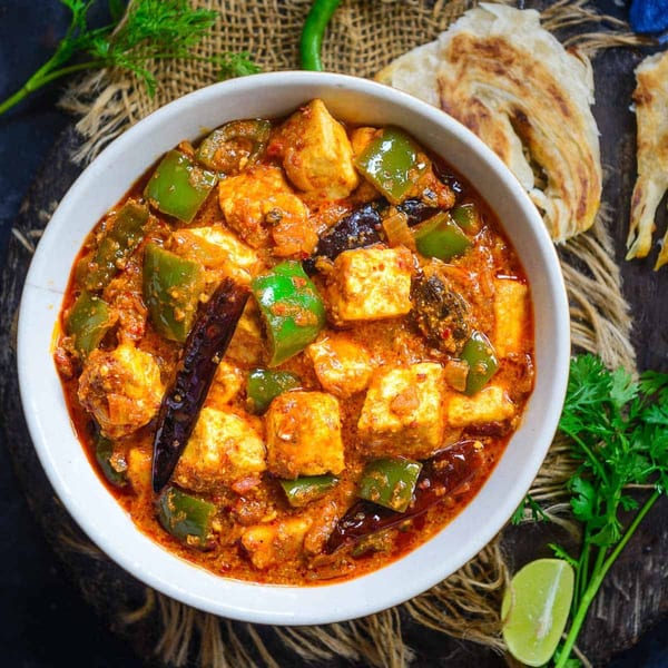 Indian paneer and bell pepper curry in a white bowl, with naan bread and lime.