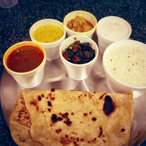 A Chaat House Indian thali with various curries, rice, and flatbread on a metal plate.