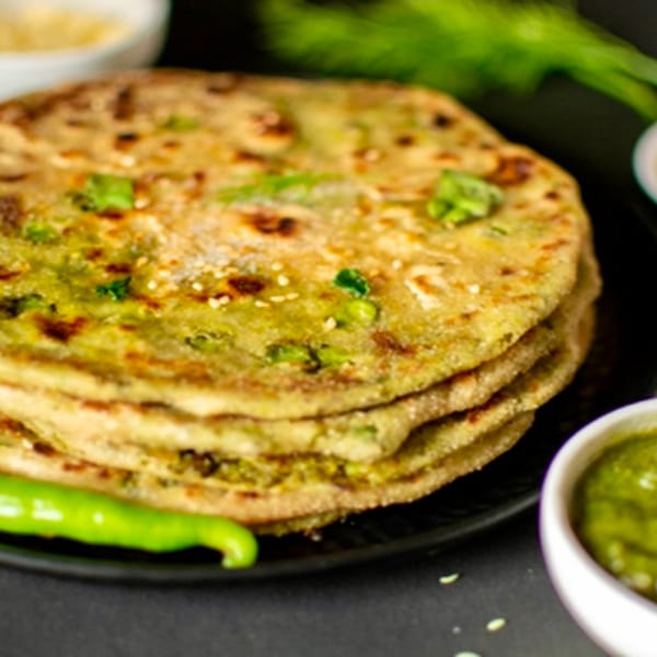 A stack of golden-brown Indian parathas, garnished with green herbs, served with green chili and chutney.