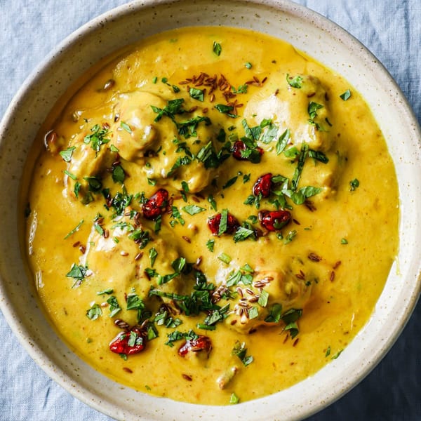 Close-up of a bowl of Indian curry, garnished with fresh herbs, cumin seeds, and red chilies.
