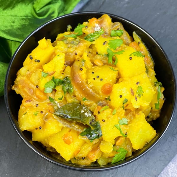 Close-up of a black bowl filled with vibrant yellow Indian pumpkin curry, garnished with fresh cilantro.