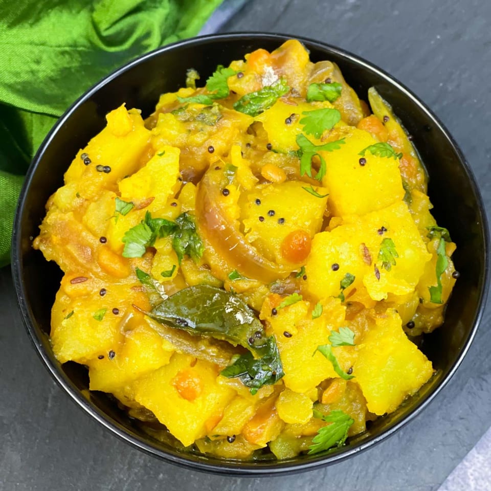 Close-up of a black bowl filled with vibrant yellow Indian pumpkin curry, garnished with fresh cilantro.