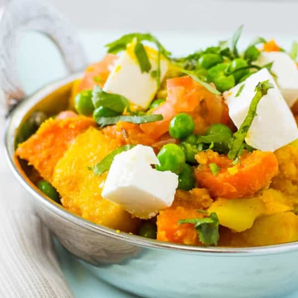 Close-up of Indian curry with paneer, peas, and carrots in a silver bowl.