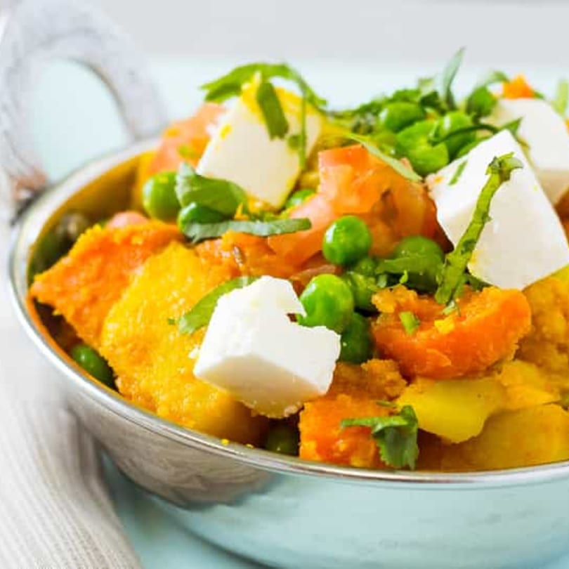 Close-up of Indian curry with paneer, peas, and carrots in a silver bowl.