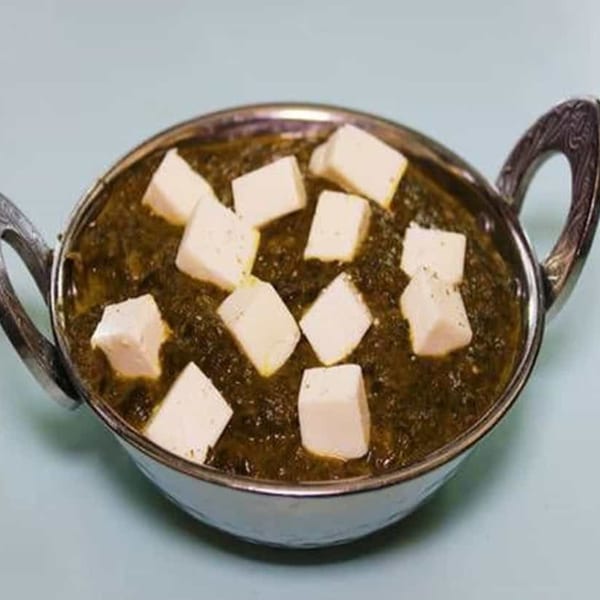 A silver bowl of Palak Paneer, a vibrant green Indian dish with white paneer cubes.