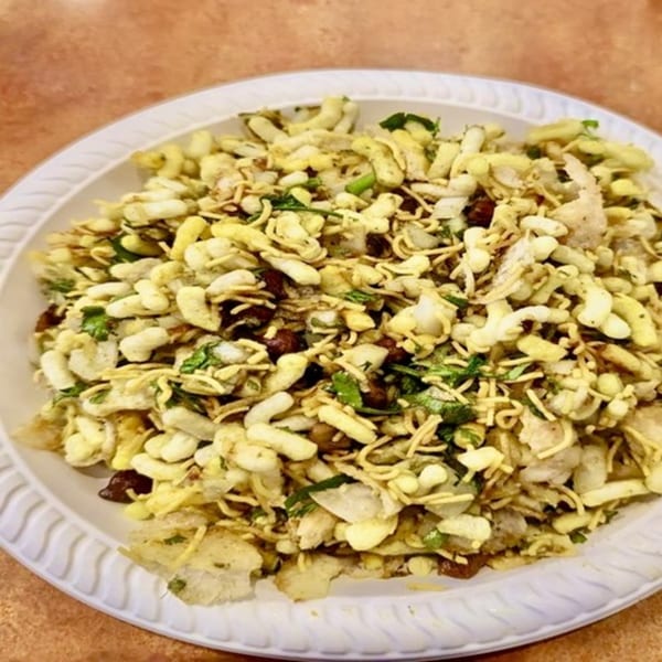 A close-up of a white plate filled with Indian Bhel Puri, a mix of puffed rice, noodles, and spices.