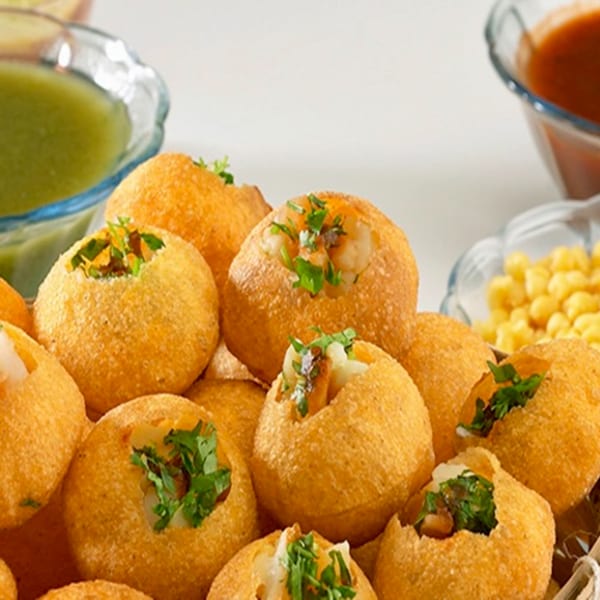 Close-up of golden pani puri shells filled with potato and chickpeas, garnished with cilantro.