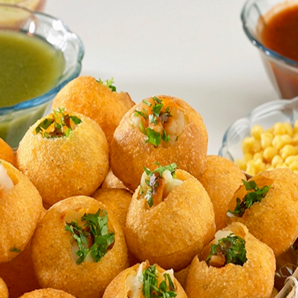 Close-up of golden pani puri shells filled with potato and chickpeas, garnished with cilantro.
