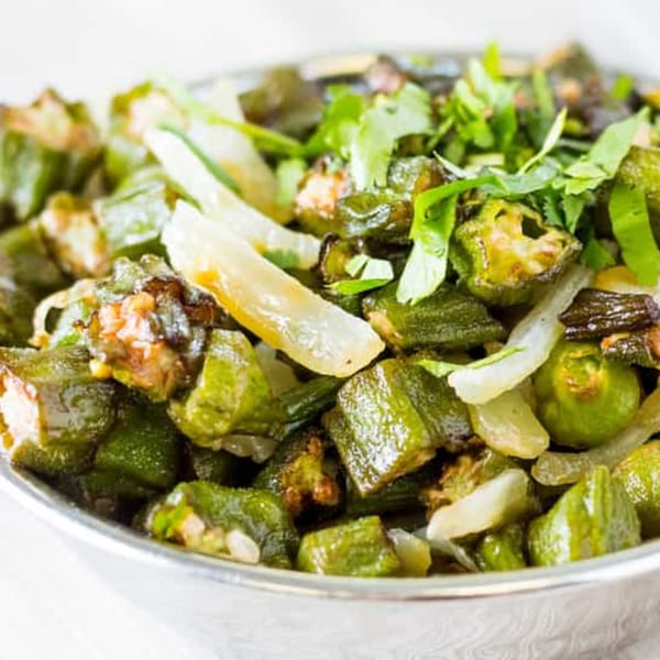 Close-up of Indian-style okra (bhindi) with onions and cilantro in a silver bowl.