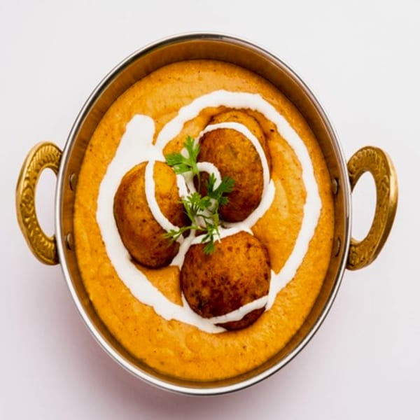 Indian Malai Kofta, fried potato and paneer balls in a creamy orange gravy, garnished with cream and cilantro.
