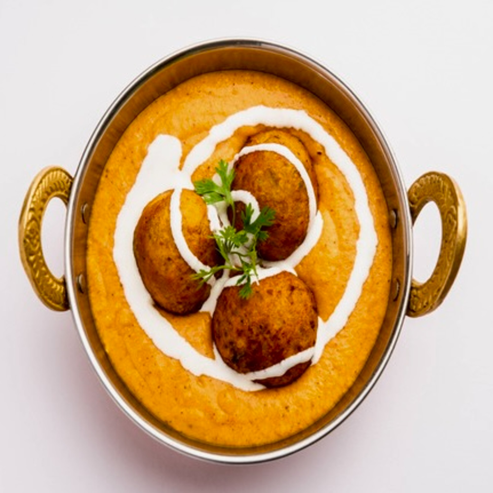Indian Malai Kofta, fried potato and paneer balls in a creamy orange gravy, garnished with cream and cilantro.