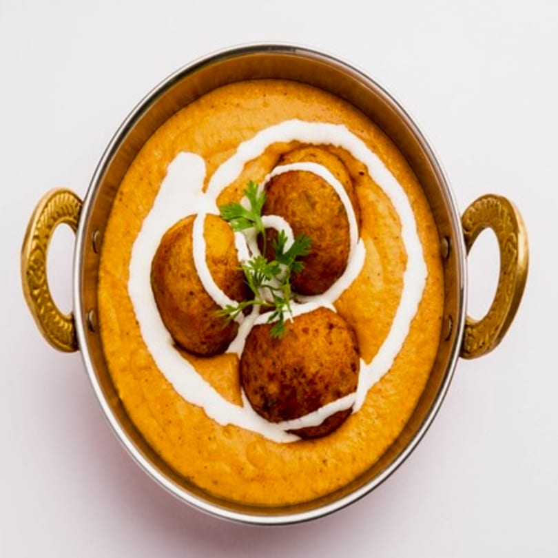 Indian Malai Kofta, fried potato and paneer balls in a creamy orange gravy, garnished with cream and cilantro.