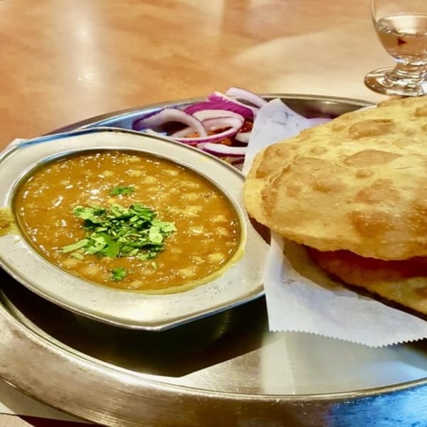 Chaat House's chole bhature, a fried bread with chickpea curry and red onions, on a metal plate.