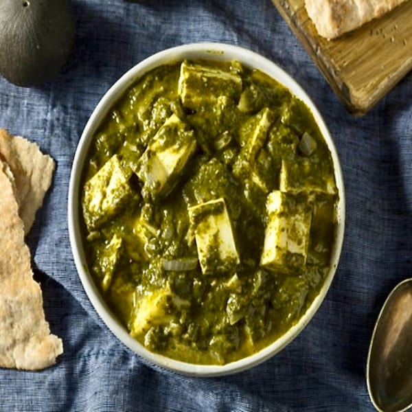 Chaat House's vibrant green Palak Paneer with paneer cubes, served with flatbread on a blue cloth.