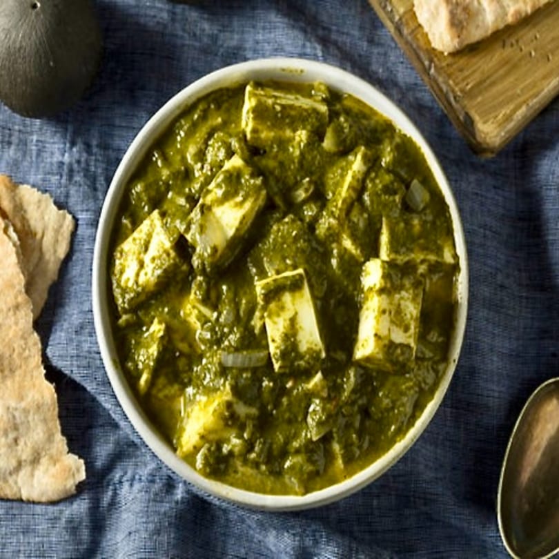 Chaat House's vibrant green Palak Paneer with paneer cubes, served with flatbread on a blue cloth.