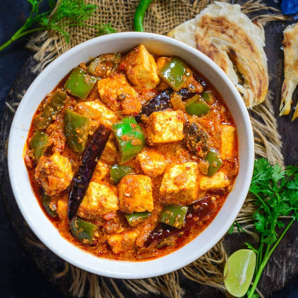 Indian paneer and bell pepper curry in a white bowl with naan bread and lime.