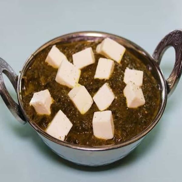 Palak Paneer, an Indian dish with spinach gravy and paneer cubes, served in a metal bowl.