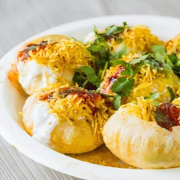 A close-up of Indian chaat, featuring crispy puris topped with yogurt, chutneys, and sev.