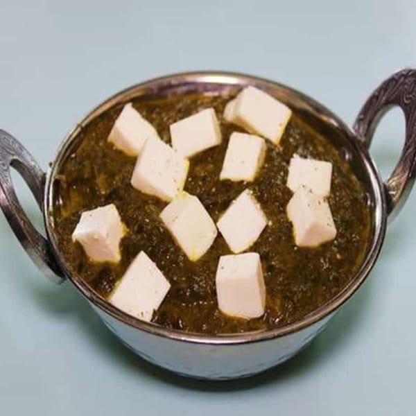 Palak Paneer, a vibrant green spinach curry with white paneer cheese cubes, in a silver bowl.